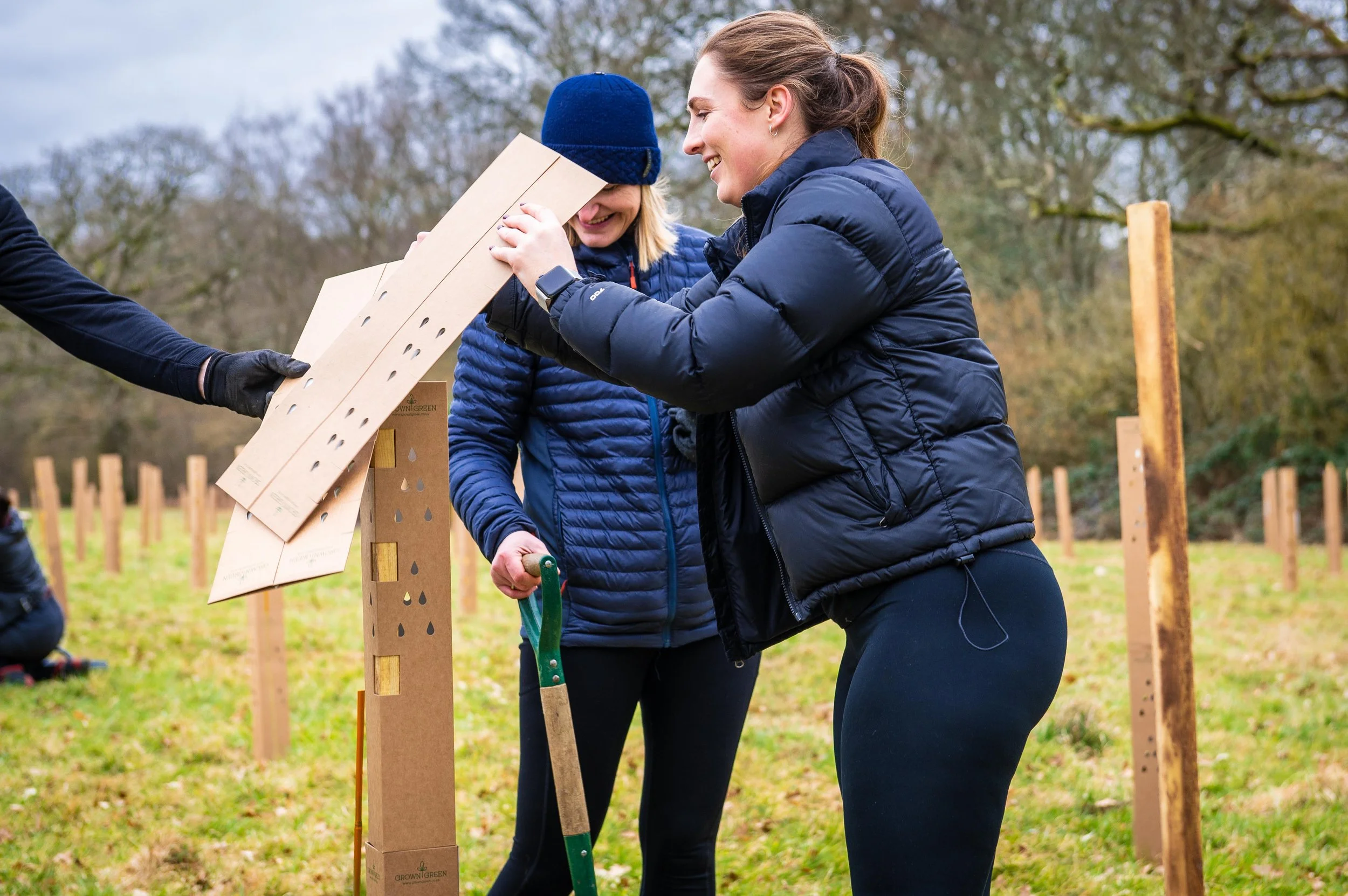 Two women smile and work together outdoors to plant a tree